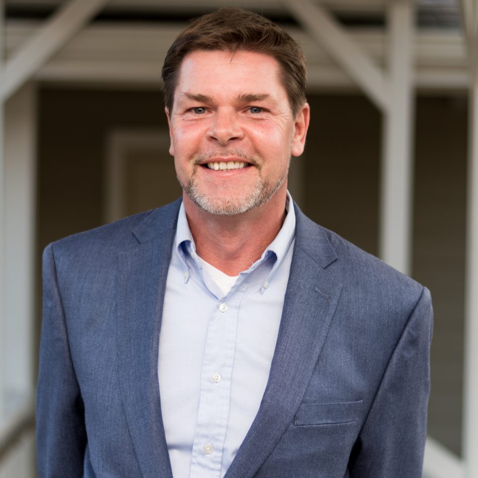 Smiling man with brown hair and a light mustache and beard wearing a blue sport coat and blue dress shirt